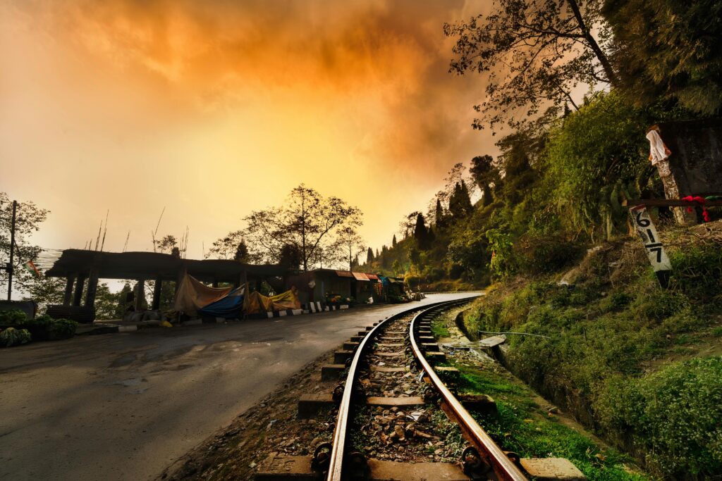 Captivating railway curves through lush Darjeeling landscape at sunset, enhancing the dramatic sky.